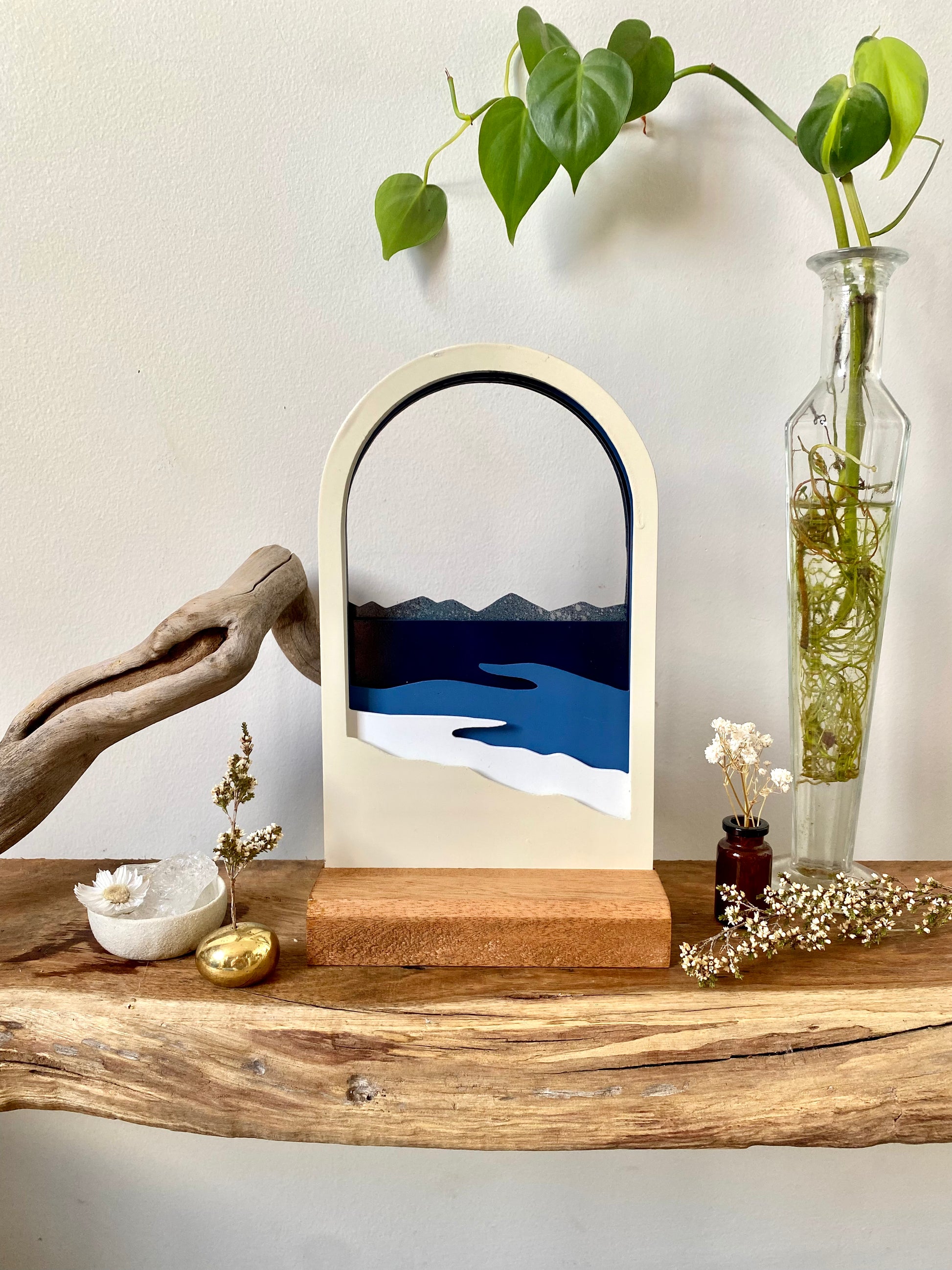 a layered steel landscape of the seaside, there are five layers from the forground to the background, the sculpture is on a rectangular wooden base.